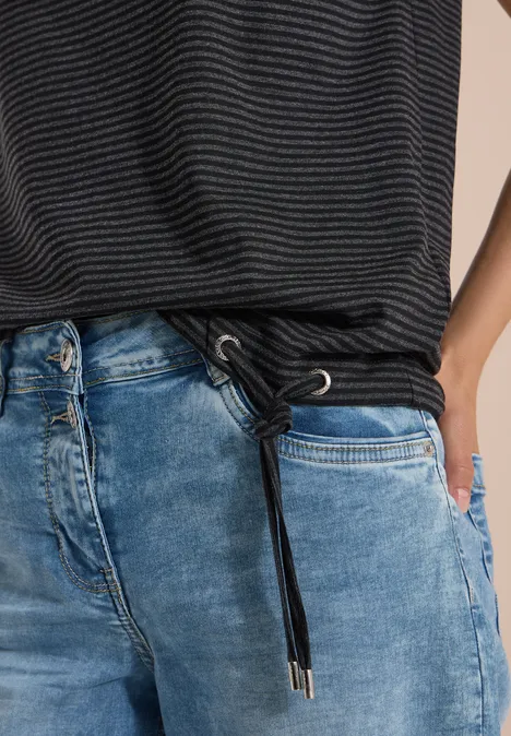 Close-up van een taille in een gestreept shirt en blauwe jeans met trekkoord, hand in zak.
