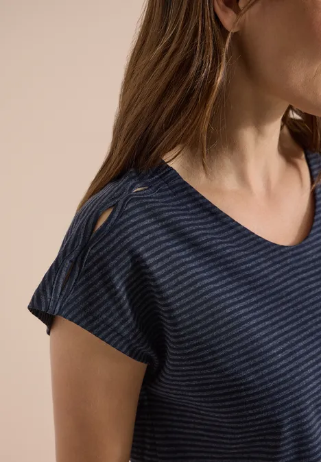 Frau in dunkelblauem, leicht gestreiftem V-Ausschnitt-T-Shirt mit Knopfdetail auf der Schulter.