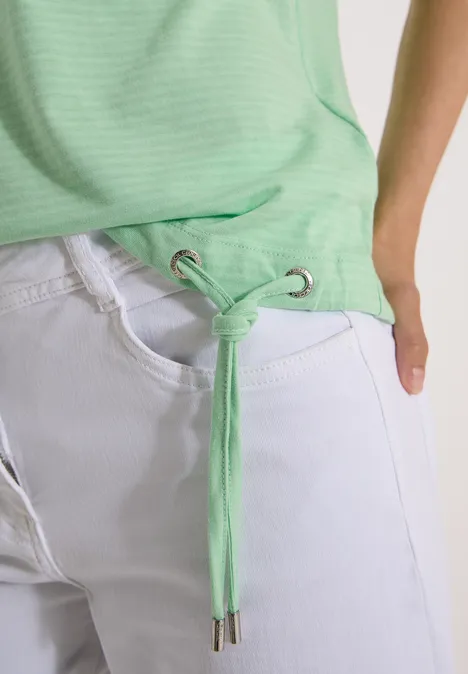 Leichtes grünes Oberteil mit Kordelzug an der Taille und weiße Jeans