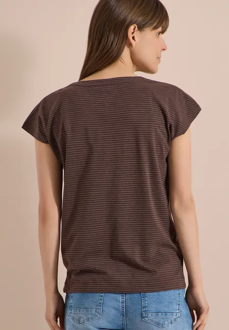 Achteraanzicht van een vrouw in een bruin gestreept T-shirt en blauwe jeans voor een effen beige achtergrond