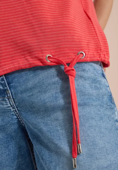 Rotes gestreiftes Shirt mit Tunnelzug-Kordel und Knoten über hellblauen Jeans.