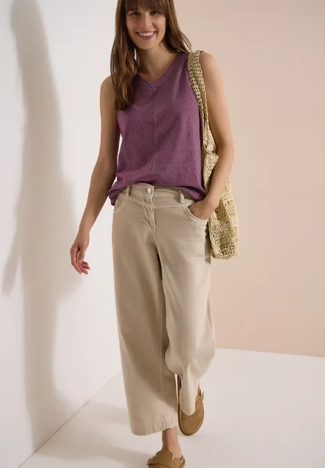 Top mit V-Neck und Streifen sweet grape red Frau trägt ärmelloses lila Top, weite beige Hose und Strohtasche in schlichtem, hellem Ambiente.