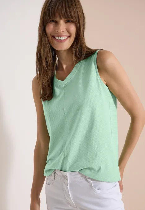Top mit V-Neck und Streifen juicy lime Frau trägt mintgrünes ärmelloses Oberteil und weiße Hose vor neutralem Hintergrund.