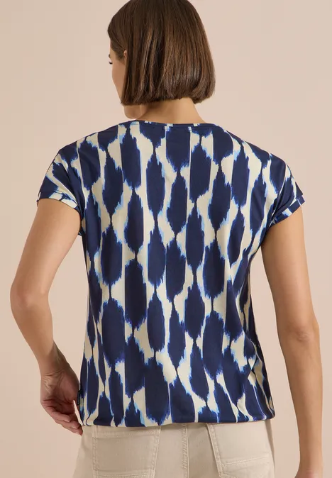 T-Shirt mit V-Neck und Spitzendetail urban dark blue Rückansicht einer Frau in kurzärmeligem T-Shirt mit blau-weißem, abstraktem Musterdruck und heller Hose.