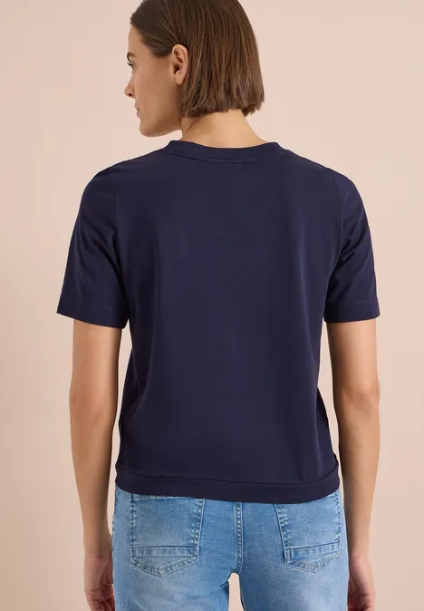 Eine Person von hinten trägt ein dunkelblaues T-Shirt und eine Jeans.