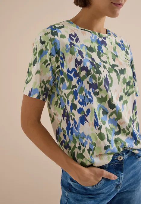 T-Shirt mit Boat Neck und Print cashmere beige Frau trägt kurzärmlige Bluse mit abstraktem Blumenmuster in Blau und Grün und blaue Jeans.