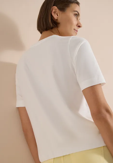 Rückansicht einer Person mit kurzem weißen T-Shirt vor beigem Hintergrund.