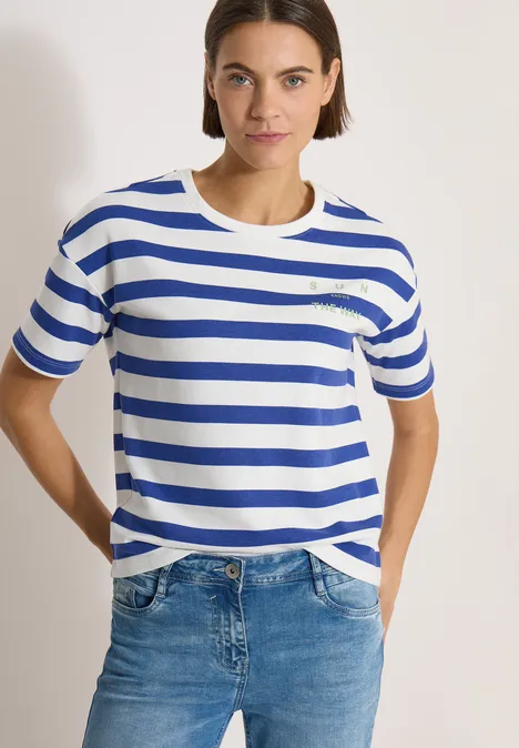 Persoon draagt wit-blauw gestreept T-shirt en spijkerbroek voor een lichte achtergrond.