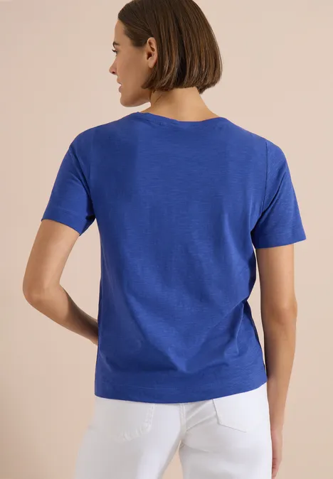 Rückansicht einer Person in blauem T-Shirt und weißer Hose.