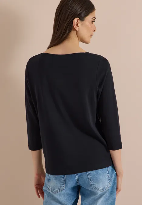 Frau von hinten, trägt schwarzes 3/4-Ärmelshirt und blaue Jeans.