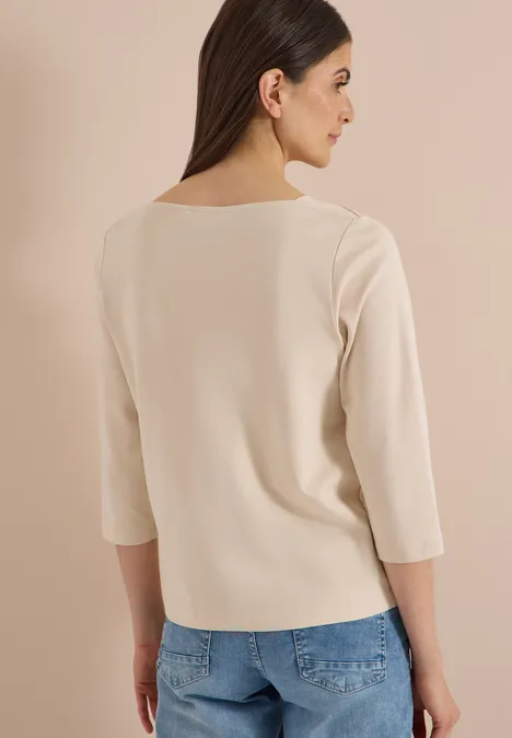 Frau in heller, taillierter 3/4-Arm-Bluse und Jeans, Rückenansicht, braune lange Haare.