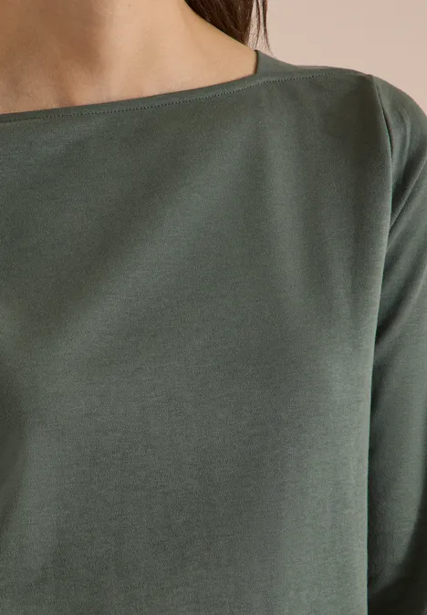 Nahaufnahme eines Oberkörpers in einem schlichten dunkelgrünen Langarmshirt mit schmalem Rundhalsausschnitt.