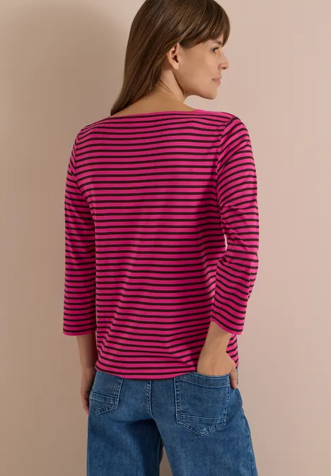 3/4-Arm Shirt mit Boat Neck und Streifen pink flash Frau von hinten in Jeans, trägt pink-schwarz gestreiftes 3/4-Arm-Shirt und schaut seitlich, vor hellem Hintergrund.