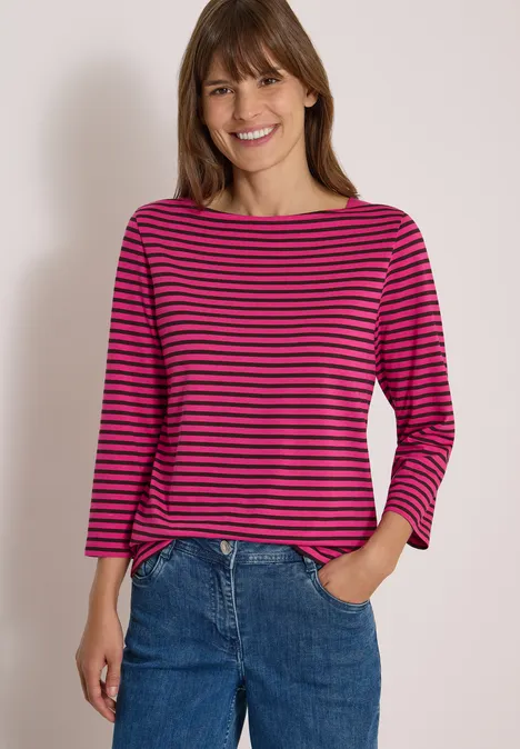 3/4-Arm Shirt mit Boat Neck und Streifen pink flash Eine Frau mit pink-blau gestreiftem Shirt und Jeans lächelt in die Kamera.