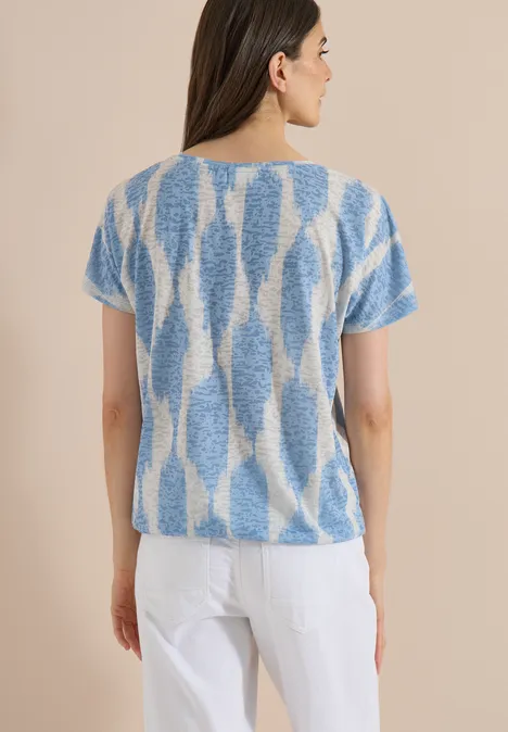 T-shirt effet délavé avec inscription urban dark blue Femme de dos portant un pull court à motifs bleus et blancs et un pantalon blanc sur fond clair.