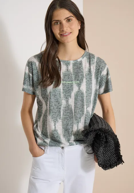 T-shirt effet délavé avec inscription deep matcha green Femme en tee-shirt à manches courtes motif vert-gris, pantalon blanc, tenant une veste noire.