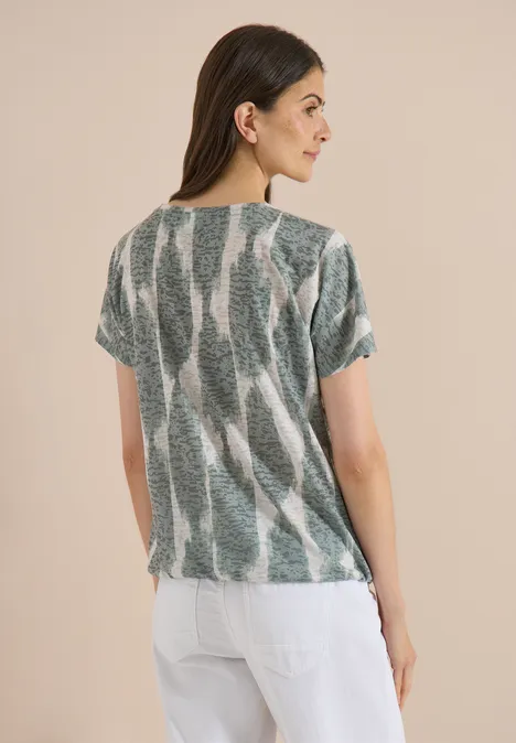 T-shirt effet délavé avec inscription deep matcha green Femme de dos aux cheveux lâchés portant un top ample à motif vert et blanc et un pantalon blanc.