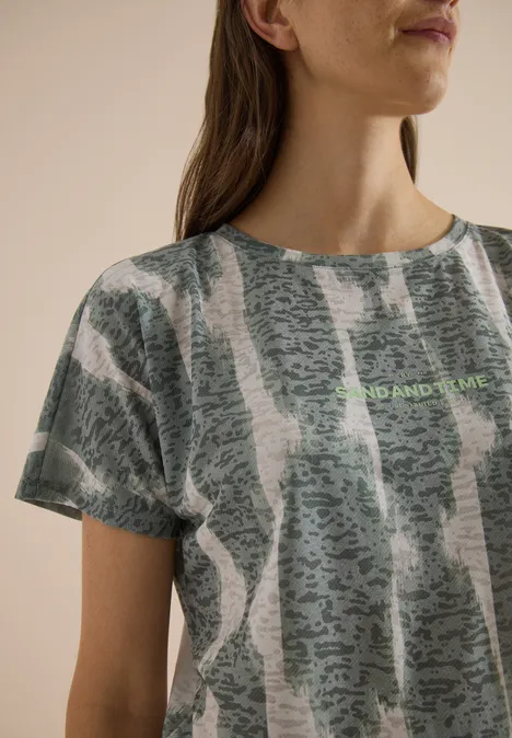 T-shirt effet délavé avec inscription deep matcha green Gros plan d'une femme en t-shirt gris-vert à motif abstrait et inscription discrète.