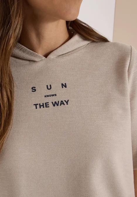 Beige Kapuzenpullover mit dunkler Aufschrift 'SUN inverses THE WAY' an einer seitlich fotografierten Person.