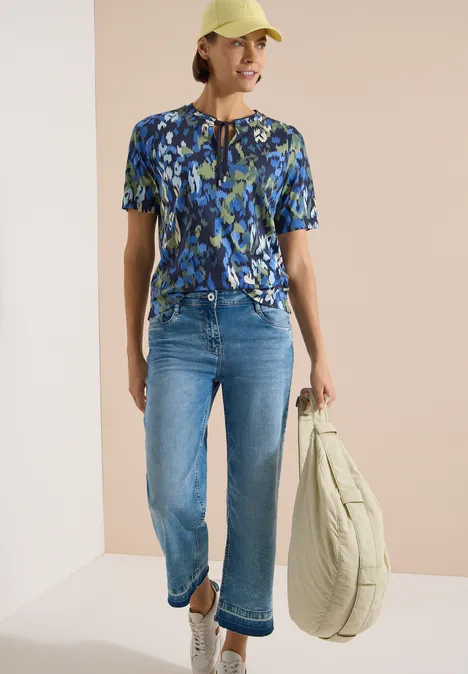 T-Shirt mit Split Neck und Print urban dark blue Dame trägt blau gemustertes Kurzarmshirt, knöchellange Jeans und eine große, weiche Umhängetasche.