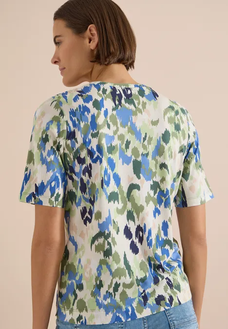 T-Shirt mit Split Neck und Print cashmere beige Rückansicht einer Frau mit kurzem braunem Haar und einer kurzärmligen Bluse mit grün-blauem abstraktem Muster.