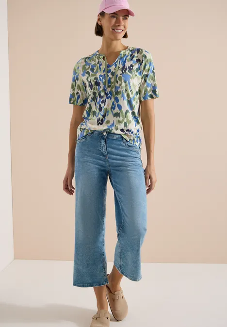 T-Shirt mit Split Neck und Print cashmere beige Frau in geblümter kurzärmeliger Bluse, weiter, knöchellanger Jeans und beigen Schuhen