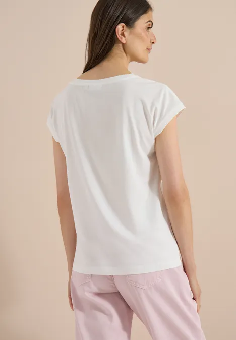 Frau von hinten in weißem T-Shirt und rosa Hose vor neutralem Hintergrund.