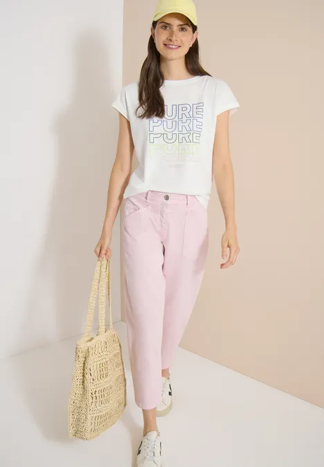 Frau in weißem T-Shirt, rosa Jeans und Basttasche.