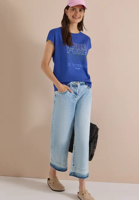 Frau trägt blaues T-Shirt mit Aufdruck und weite hellblaue Jeans-Culottes.