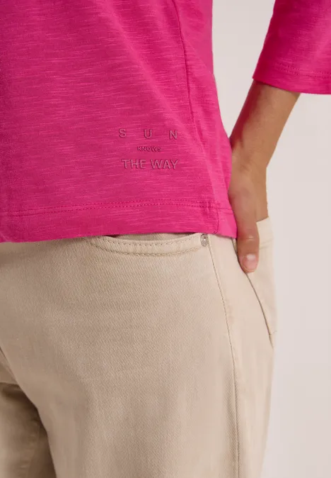 3/4-Arm Shirt in Unifarbe mit V-Neck pink flash Nahaufnahme eines Oberkörpers in pinkem Shirt und beigefarbenen Hosen, Hand steckt in Hosentasche.
