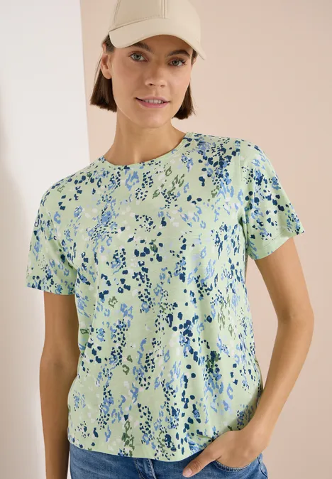 T-Shirt mit Rundhals und Print raw matcha lime Eine Person trägt ein kurzärmeliges T-Shirt mit grün-blauem Muster und steht mit einer Hand in der Hosentasche.