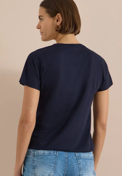 T-Shirt mit Split Neck in Unifarbe urban dark blue Frau im Profil von hinten mit dunkelblauem T-Shirt und Jeans vor neutralem Hintergrund.