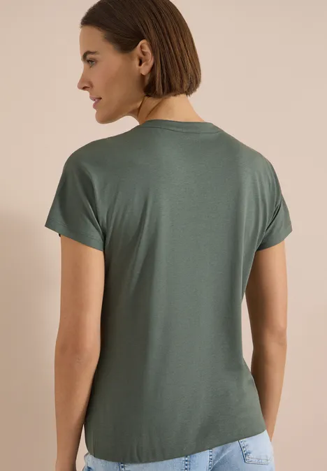 T-Shirt mit Split Neck in Unifarbe dried olive green Frau von hinten in schlichtem grünem T-Shirt vor beigem Hintergrund.