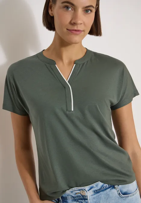 T-Shirt mit Split Neck in Unifarbe dried olive green Frau in dunkelgrünem T-Shirt mit V-Ausschnitt und Kontrastkante, dazu hellblaue Jeans.