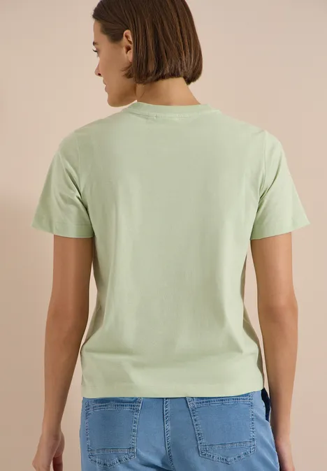 Person steht mit dem Rücken zur Kamera, trägt hellgrünes T-Shirt und blaue Jeans.