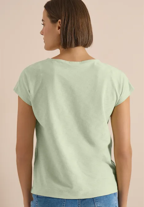 Shirt met boothals en structuur raw matcha lime Persoon gezien van achteren met lichtgroen T-shirt, neutrale achtergrond en halflang haar.