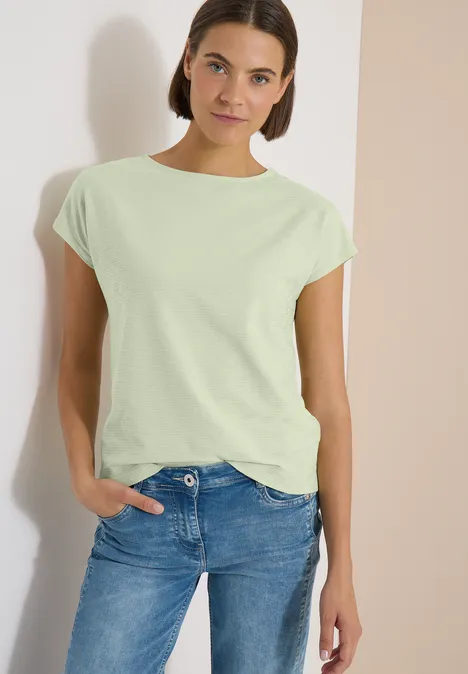 Shirt met boothals en structuur raw matcha lime Vrouw in lichtgroen T-shirt met opgerolde mouwen en een blauwe jeans, hand in de zak.