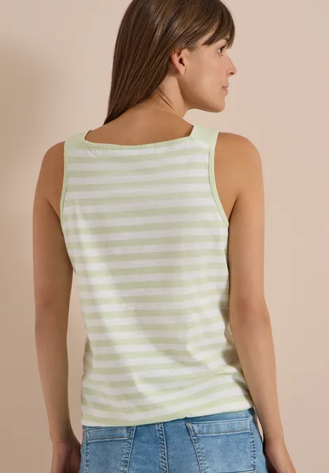 Top mit Rounded V-Neck und Streifen raw matcha lime Frau von hinten im ärmellosen, hellgrün-weiß gestreiften Top und blauen Jeans vor beiger Wand.