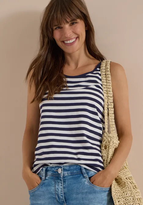 Top mit Rounded V-Neck und Streifen urban dark blue Lächelnde Frau in gestreiftem Top, Jeans und Strohtasche vor neutralem Hintergrund.
