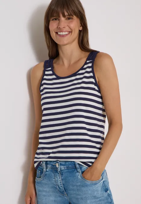 Top mit Rounded V-Neck und Streifen urban dark blue Frau in blau-weiß gestreiftem Tanktop und Jeans, lächelnd mit Händen in den Taschen.