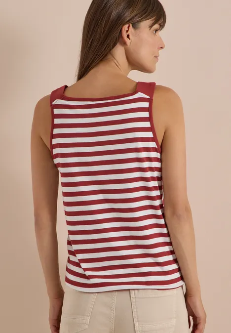 Top mit Rounded V-Neck und Streifen russet red Frau in rotem-weiß gestreiftem Tanktop und hellen Hosen, seitlich abgewandt vor neutralem Hintergrund.