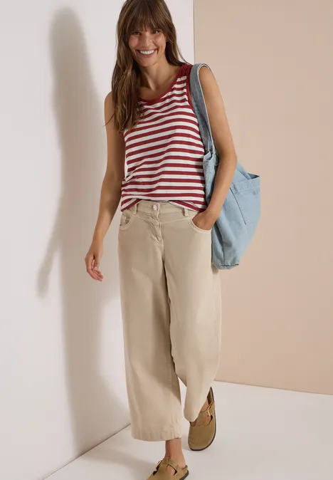 Top mit Rounded V-Neck und Streifen russet red Eine lächelnde Frau in rot-weiß gestreiftem Top, weiten beigen Hosen und mit blauer Tasche vor hellem Hintergrund.