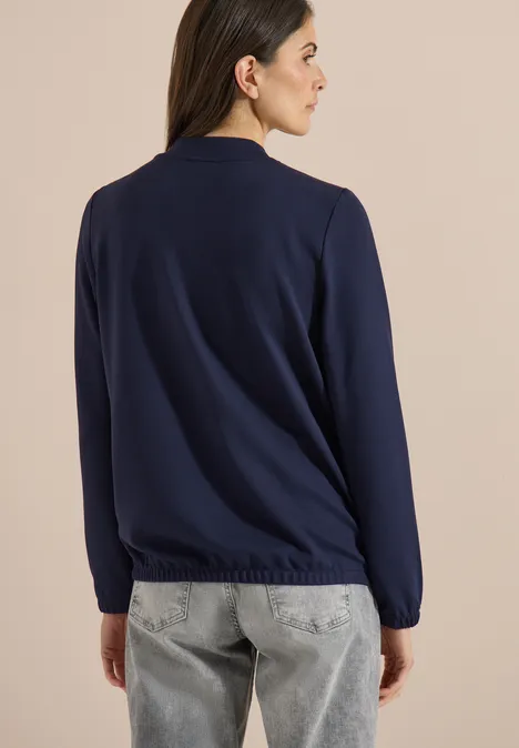Vue de dos d'une personne portant un pull bleu marine et un jean gris clair sur fond neutre.