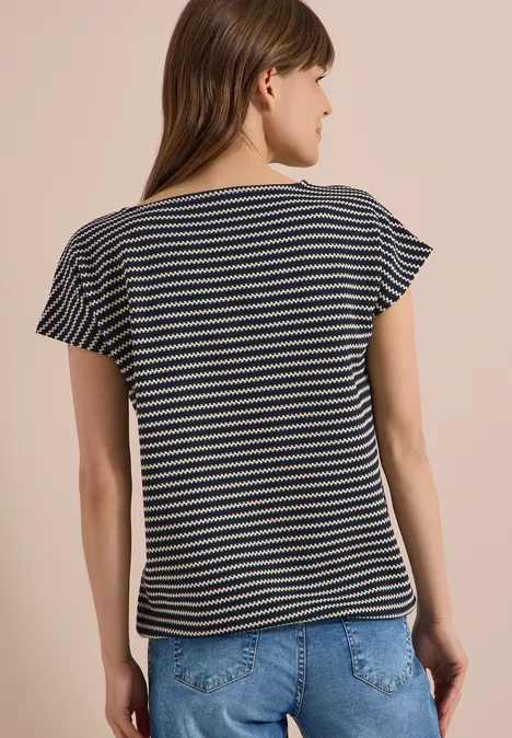 Een vrouw van achteren in een blauw-wit gestreept shirt en spijkerbroek voor een beige achtergrond.
