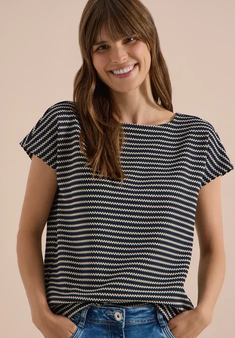 Een vrouw draagt een gestreept T-shirt met korte mouwen voor een lichte achtergrond.