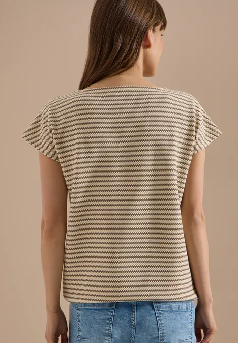 Vrouw van achteren in een gestreept shirt met korte mouwen en een spijkerbroek voor een effen achtergrond.