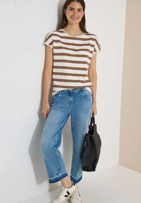 T-shirt à encolure bateau et boutons décoratifs creamy mocha Femme portant un t-shirt rayé, un jean large bleu et des baskets blanches, tenant un sac noir duveteux.