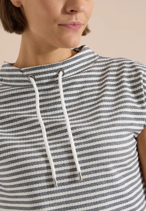 Vrouw draagt een grijs-wit gestreept shirt met korte mouwen en losse koordkraag.