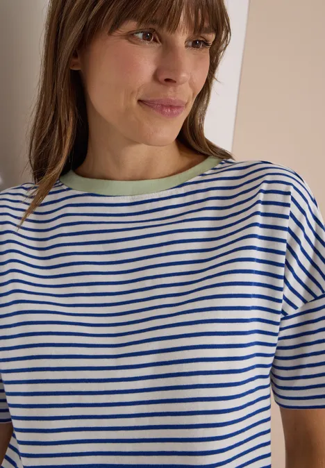 Frau im gestreiften T-Shirt mit blau-weißen Streifen und grünem Kragen lächelt leicht.
