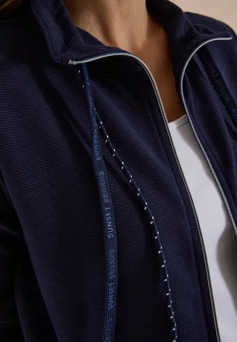 Nahaufnahme einer Person in dunkelblauer Zip-Jacke über weißem Top.